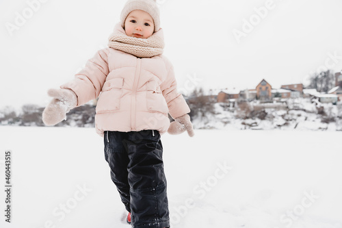 Winter cheerful little child playing throws up snow outdoors. The girl is lying in the snow, playing and having fun.