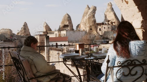 Back view of mother and daughter sitting on terrace in Goreme village. Woman and girl sitting together in cafe and enjoying amazing view in Cappadocia, Turkey photo