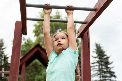One active young girl, fit sporty child climbing, outdoor exercise, hanging on a bar on a playground, portrait, closeup. Children and healthy physical activities in summer simple concept, lifestyle © Tomasz