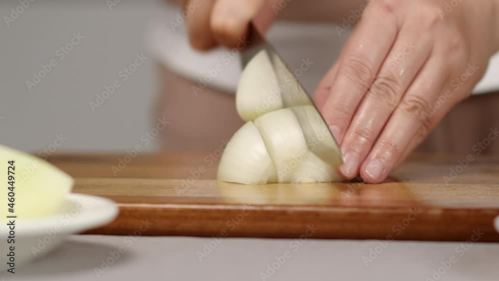 cook cuts the onion into large pieces with a knife on a wooden board close-up cook cuts the onion into large pieces with a knife on a wooden board close-up