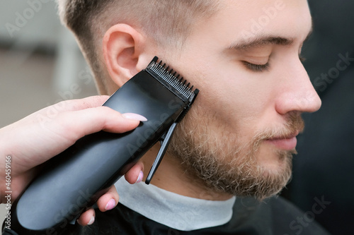 haircut process of blond young man with hair trimmer in armchair in barbershop salon