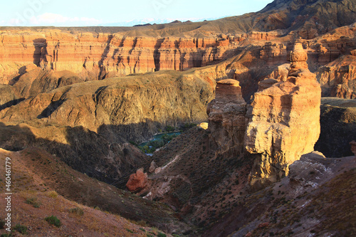 Top view of the red Charyn canyon with the river, bizarre reliefs of the canyon slopes at sunset in summer, the canyon slopes are covered with grass, trees grow on the river bank
