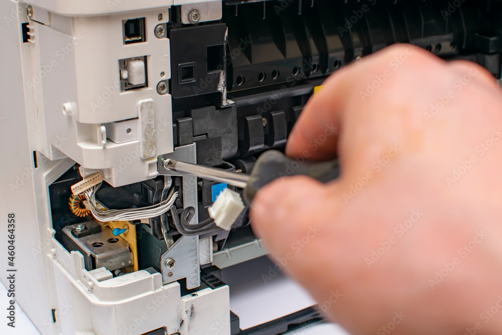 close up, a view of the tip of a phillips screwdriver, with which the master hand unscrews the bolt of the disassembled printer thermoblock, fuser