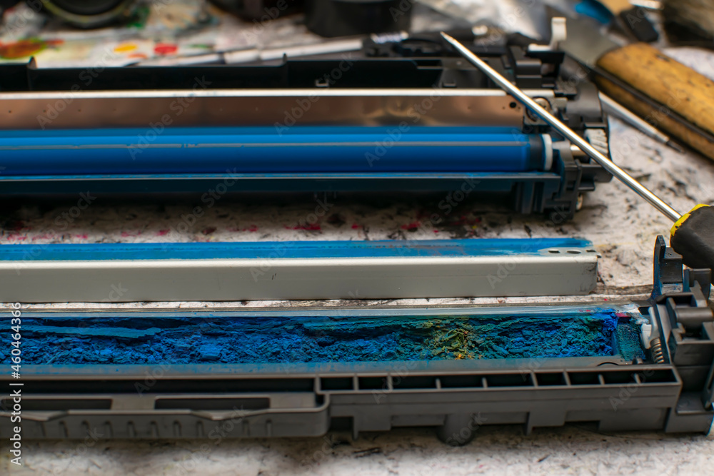 Obraz premium a view of colored toner in the hopper of the blue laser printer cartridge, which lies against the background of the disassembled unit next to a screwdriver, tools on the service work table