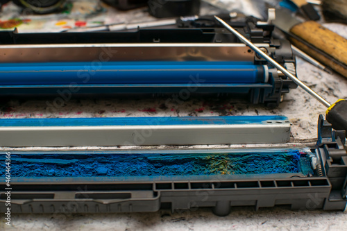 a view of colored toner in the hopper of the blue laser printer cartridge, which lies against the background of the disassembled unit next to a screwdriver, tools on the service work table