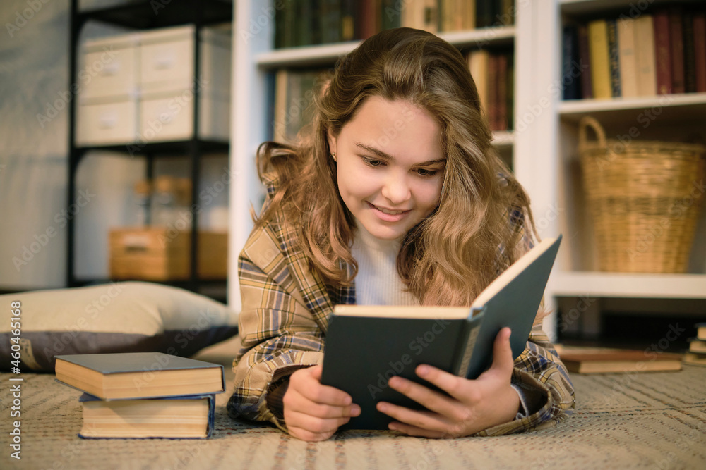 girl sits on the couch and reads a book, a tablet and headphones lie next to it. modern teenager at home. teen literature concept. girl sits on the couch and reads a book, a tablet and headphones lie next to it. modern teenager at home. teen literature concept.