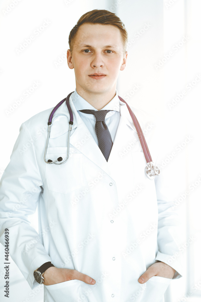 Man-doctor standing straight in sunny clinic. Medicine concept Man-doctor standing straight in sunny clinic. Medicine concept