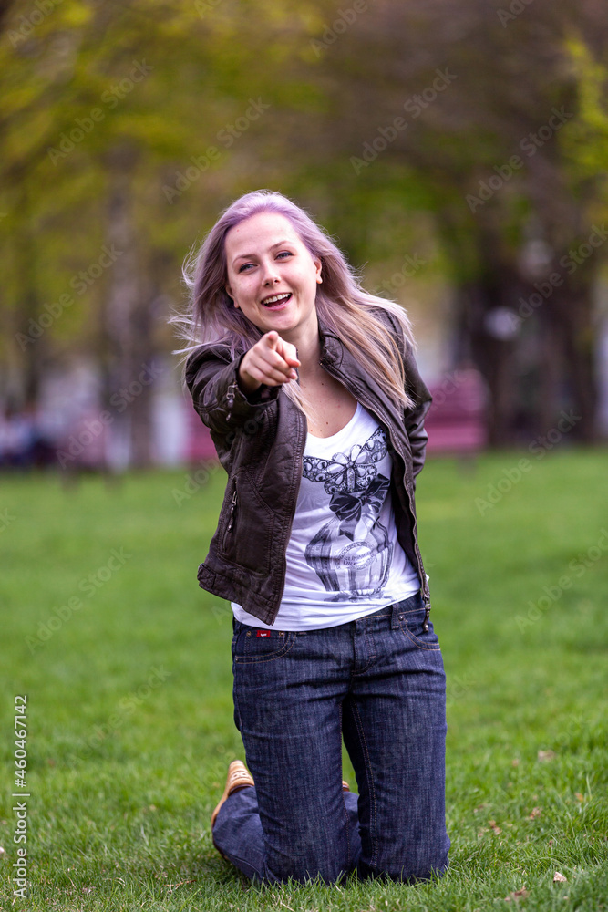 Fototapeta premium Young blonde with blue eyes in the park on green grass flirts with the camera