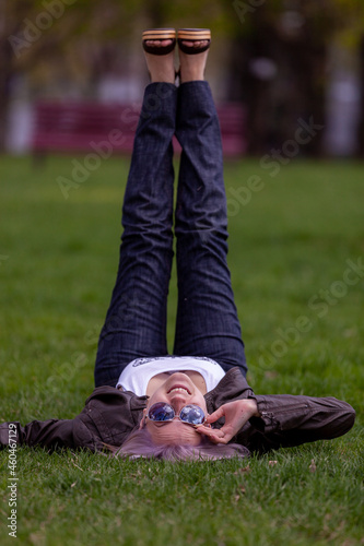 Young blonde with blue eyes in the park on green grass flirts with the camera