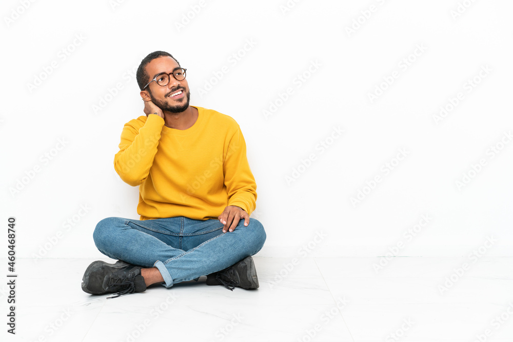 Young Ecuadorian man sitting on the floor isolated on white wall thinking an idea Young Ecuadorian man sitting on the floor isolated on white wall thinking an idea