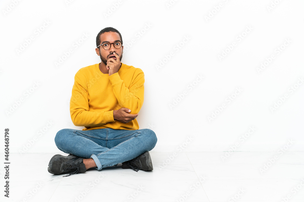 Young Ecuadorian man sitting on the floor isolated on white wall surprised and shocked while looking right Young Ecuadorian man sitting on the floor isolated on white wall surprised and shocked while looking right