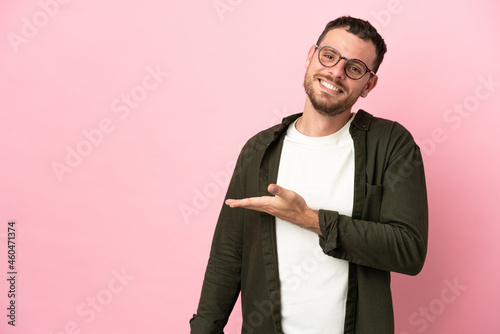 Young Brazilian man isolated on pink background presenting an idea while looking smiling towards