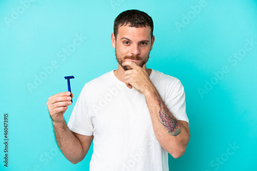 Brazilian man shaving his beard isolated on blue background thinking