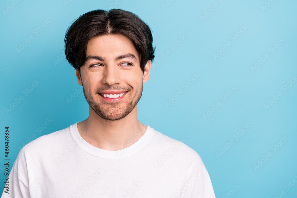 Photo of nice young brunet guy look empty space wear white t-shirt isolated on blue color background
