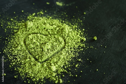 Matcha green tea in the shape of heart on black background with free space for text.