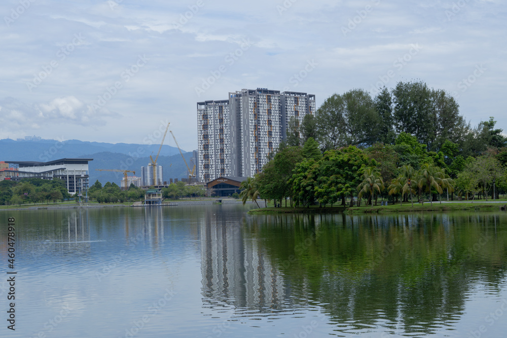 peaceful scene of cityscape in Kepong, Kuala Lumpur, Malaysia. Greenery woods, high-rise buildings, hills and clear cloud sky in background with reflection on water. 