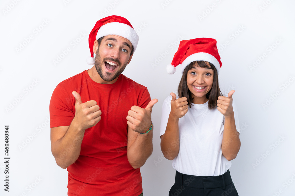Young couple with christmas hat isolated on white background giving a thumbs up gesture with both hands and smiling Young couple with christmas hat isolated on white background giving a thumbs up gesture with both hands and smiling