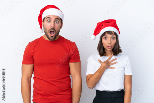 Young couple with christmas hat isolated on white background with surprise and shocked facial expression