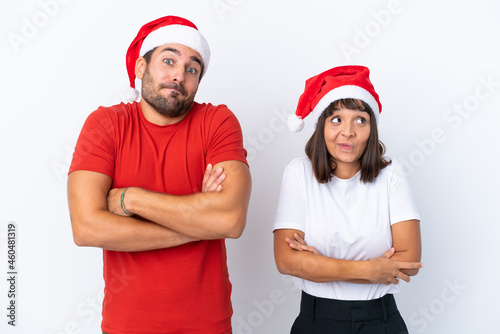 Young couple with christmas hat isolated on white background making doubts gesture while lifting the shoulders