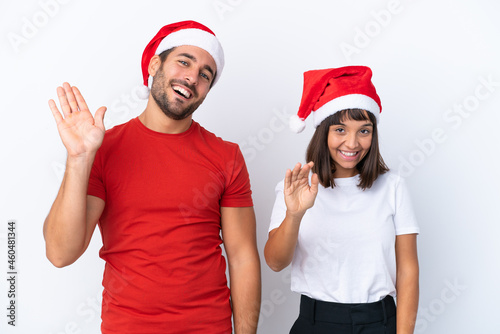Young couple with christmas hat isolated on white background saluting with hand with happy expression