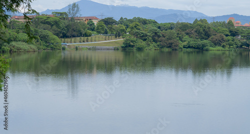 Beautiful and peaceful view of a lake in the outskirt of Kepong, Kuala Lumpur, Malaysia. Still water, reflection of green trees being the main focus, hills and clear cloud sky in background. 