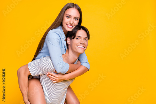 Portrait of attractive cheerful couple piggy backing having fun rest free time isolated over vivid yellow color background