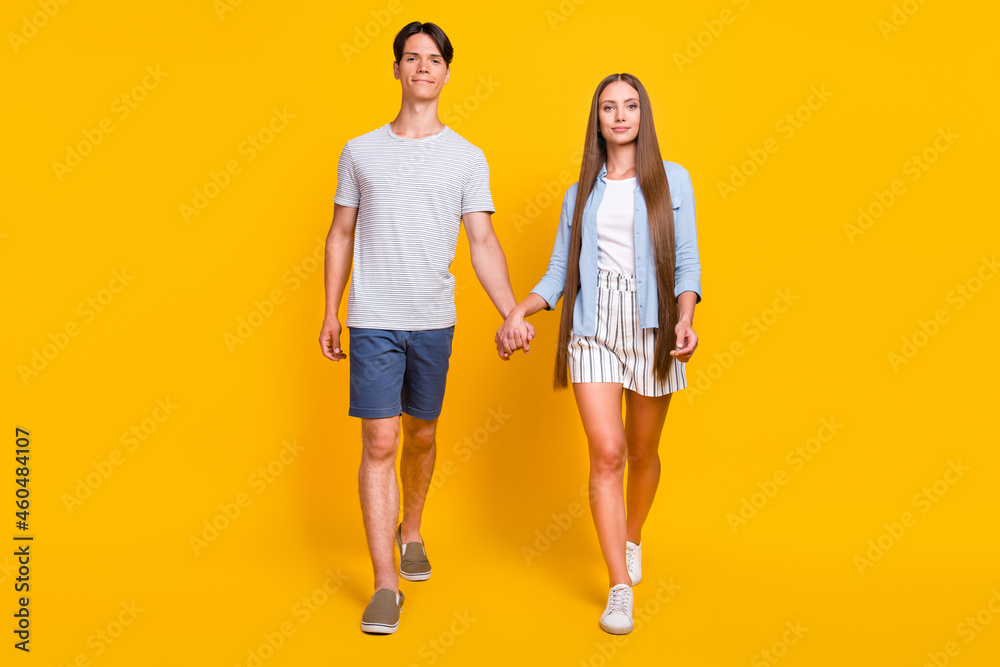 Full length body size view of attractive cheery couple going holding hands isolated over bright yellow color background Full length body size view of attractive cheery couple going holding hands isolated over bright yellow color background