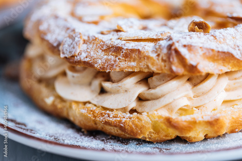 Dessert called Paris Brest on a grey background with powder sugar and almond leaves and almond creme between photo