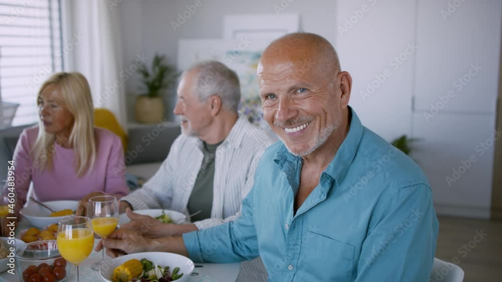 Senior man with friends having party indoors, eating at the table and looking at camera. Senior man with friends having party indoors, eating at the table and looking at camera.