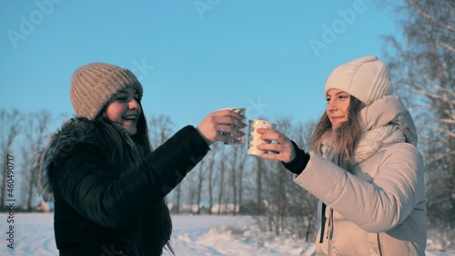 Quadro em tela Two friends drink hot tea in winter and clink glasses hugging.