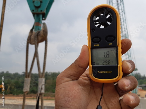 LAMPUNG, INDONESIA - AUGUST 20, 2018: A construction worker's hand is holding an anemometer during the girder lifting process during the day.