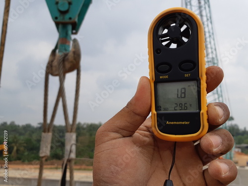 Photos LAMPUNG, INDONESIA - AUGUST 20, 2018: A construction worker's hand is holding an anemometer during the girder lifting process during the day