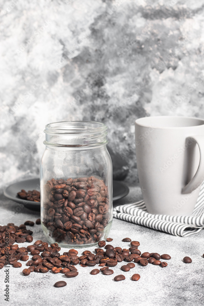 Jar of coffee beans with a grey mug at the back Jar of coffee beans with a grey mug at the back