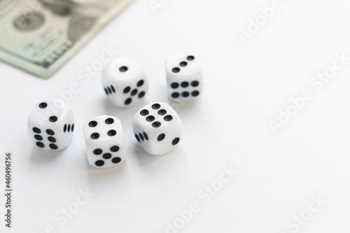 Dice and blurred 100 US dollar on white. Fortune, gaming addiction. Playing cube with numbers. Items for board games. Flat lay, top view, copy space.