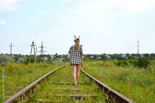 A girl in a plaid shirt and cap walks along the sleepers of an abandoned railway. a walk in the fresh air on a clear summer day