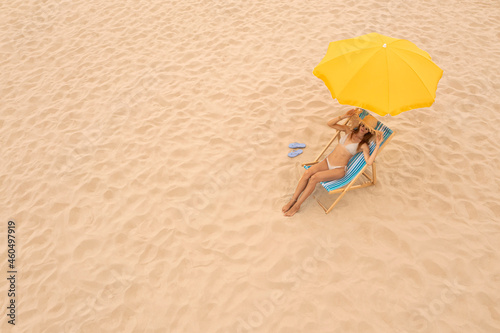 Woman resting in sunbed under yellow beach umbrella at sandy coast, space for text