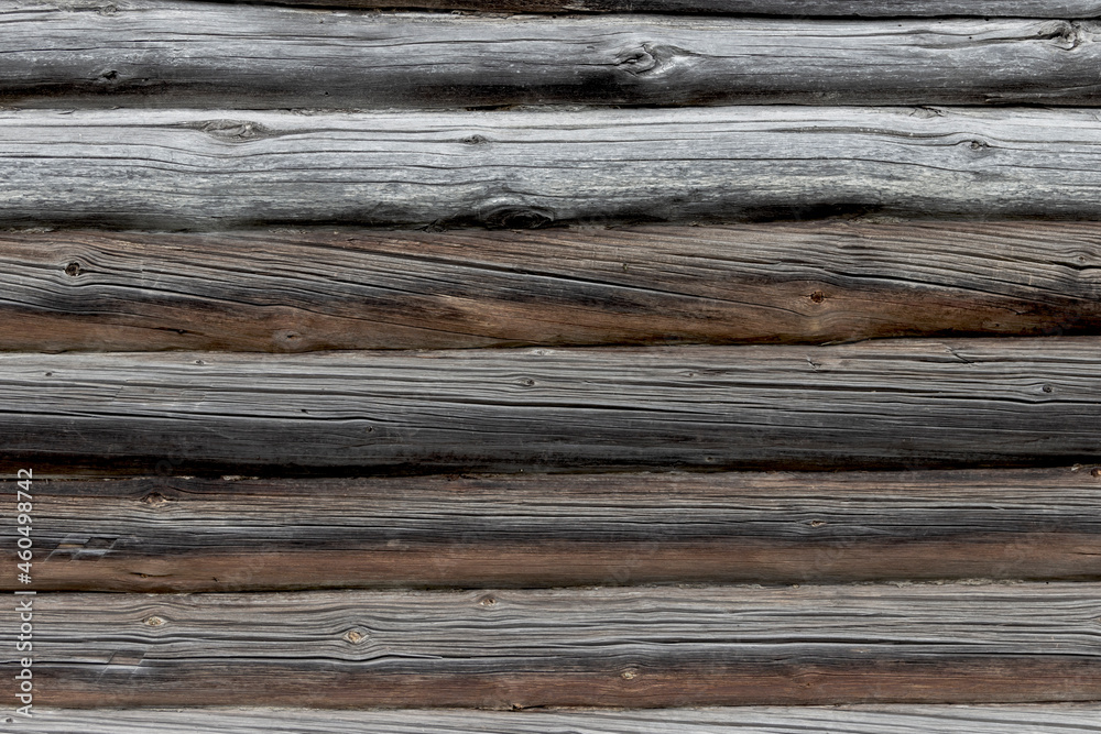The wall of an old wooden house made of darkened weathered logs. Traditional Russian log hut.