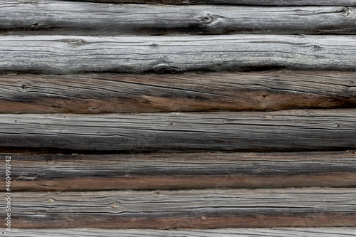 The wall of an old wooden house made of darkened weathered logs. Traditional Russian log hut.