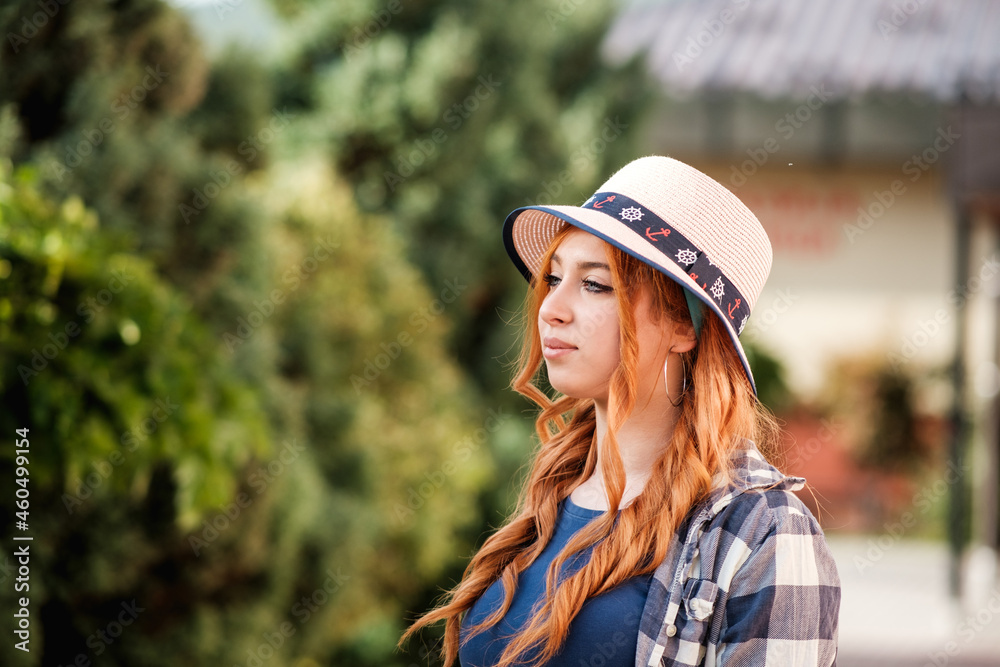a red-haired girl with a hat in the park looks to the side