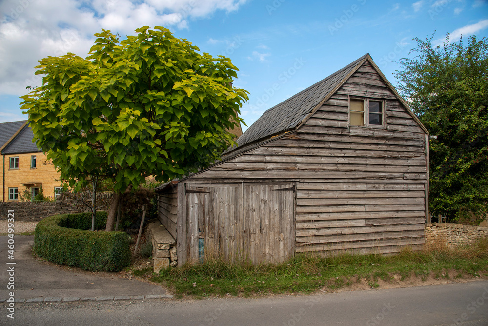 Obraz premium Guiting Power, Gloucestershire, England, UK. 2021. An old wooden barn with small garage doors in the rural Cotswolds village of Guiting Power.