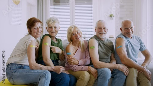 Group of senior friends showing plaster on arm indoors, covid-19 vaccination concept. photo