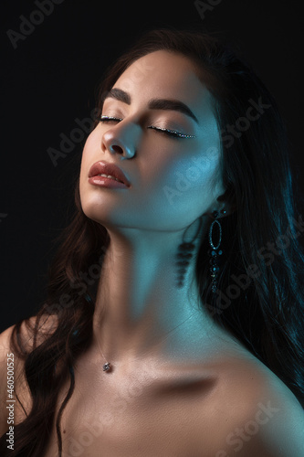 Close up portrait. Young beautiful girl with long dark hair and perfect make up in blue backlight. Studio shot.