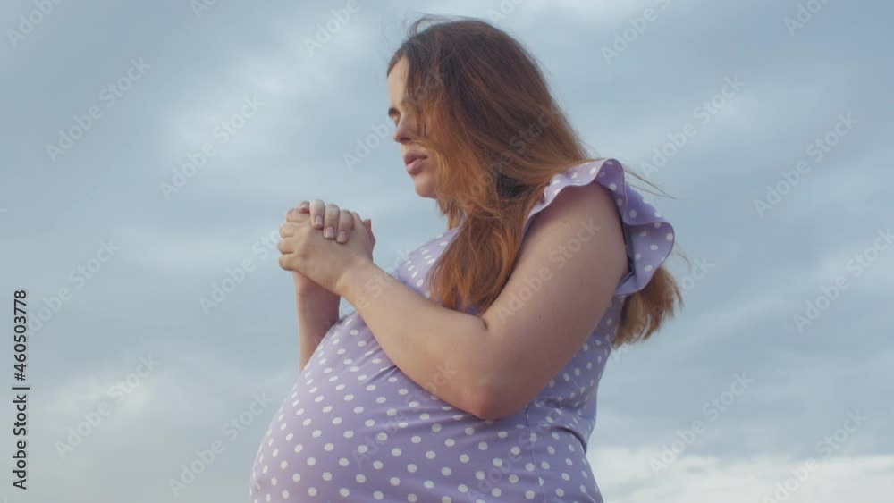 young pregnant woman folded her hands in pray to God standing alone in field against of cloudy sky, future mother walking on nature young pregnant woman folded her hands in pray to God standing alone in field against of cloudy sky, future mother walking on nature
