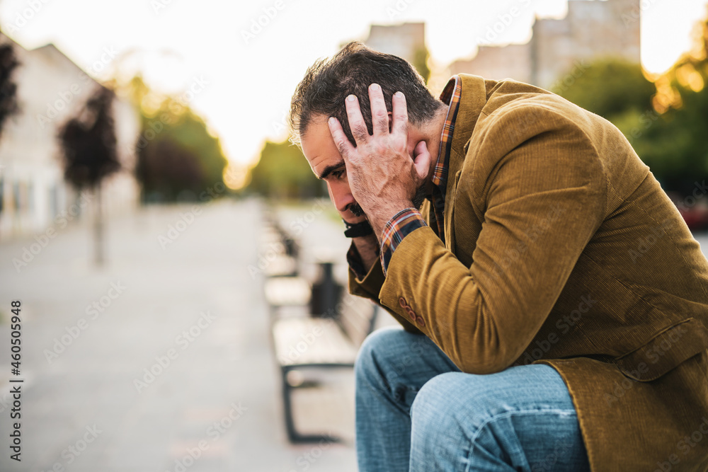 Depressed businessman having headache and sitting on a bench in the city street. Depressed businessman having headache and sitting on a bench in the city street.