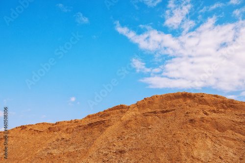 Large pile of industrial sand, stockpiled and prepared for use in construction and road construction, against a blue sky