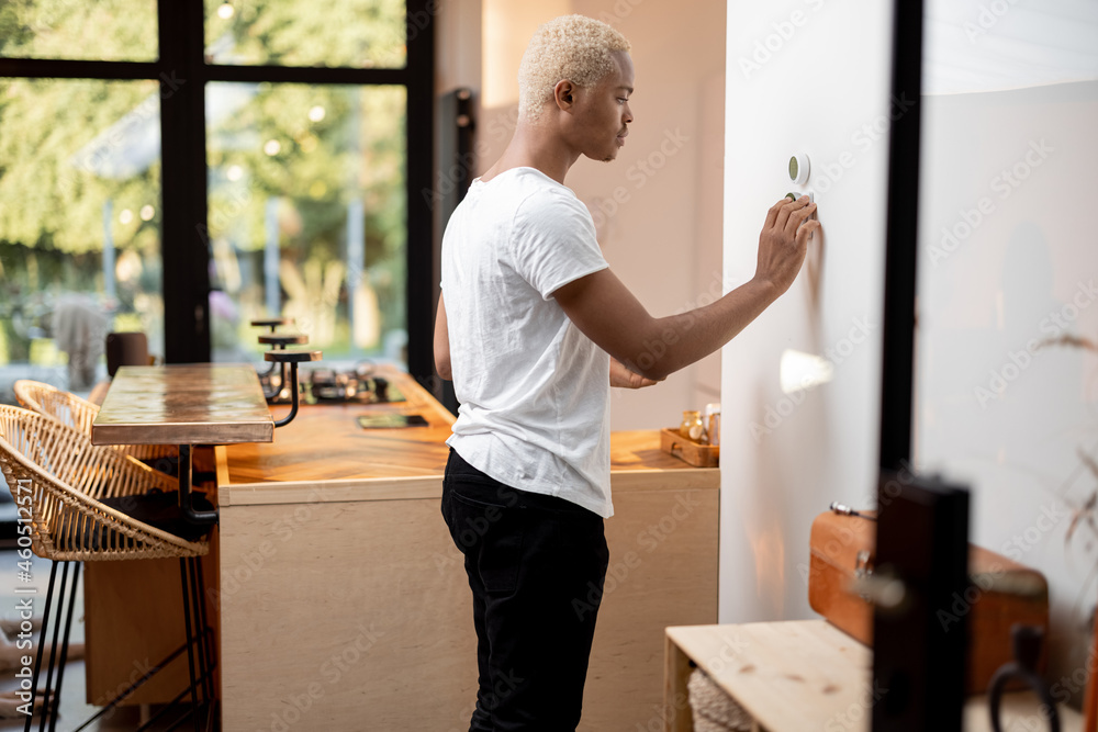 Black man choosing temperature on thermostat. Young focused guy pushing  button on smart home system. Concept of modern domestic lifestyle. Interior  of kitchen in modern apartment. Stock Photo | Adobe Stock