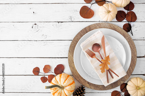 Autumn harvest or thanksgiving dinner table setting with plates, flatware, napkin and fall decor. Overhead view corner border on a white wood background with copy space.
