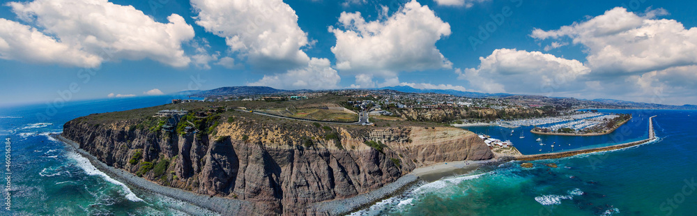 a stunning aerial panoramic shot of the deep blue ocean water and the sandy beach and the boats on the harbor with beach front homes and blue sky and clouds in Dana Point California - obrazy, fototapety, plakaty 
