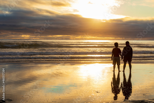 A mother and son travelling together along the Cannon Beach in Oregon looking outwards towards the horizon during a golden sunset