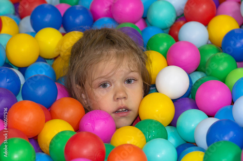 Head of sad caucasian little girl of five years old among multicolor balls in play center